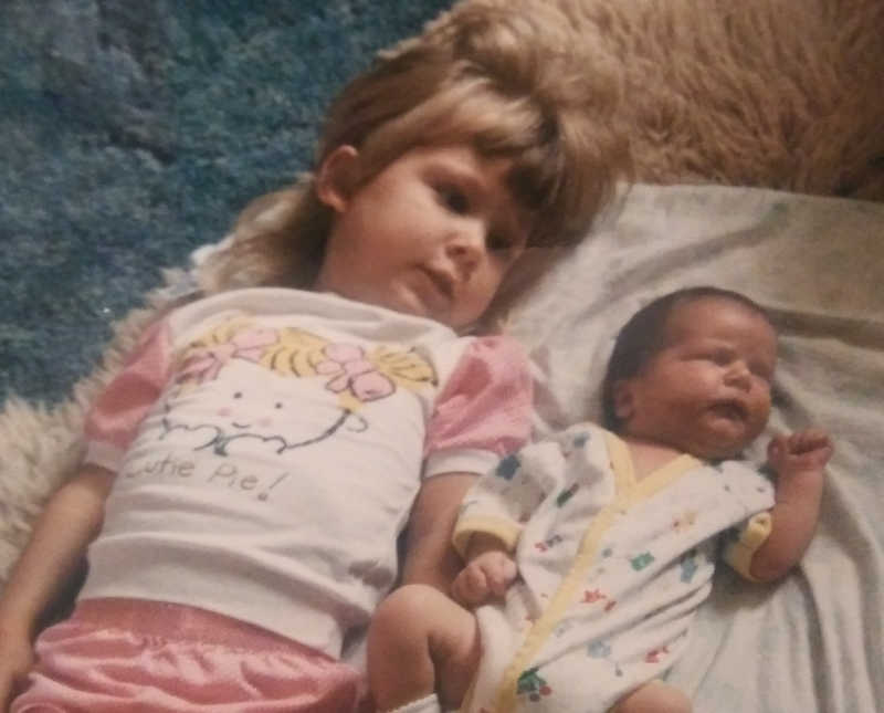 Little girl lays on back on floor with her baby sibling laying beside her