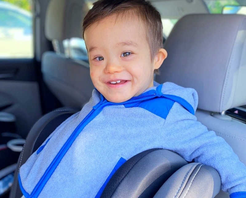 Little boy with down syndrome smiles as he sits in car
