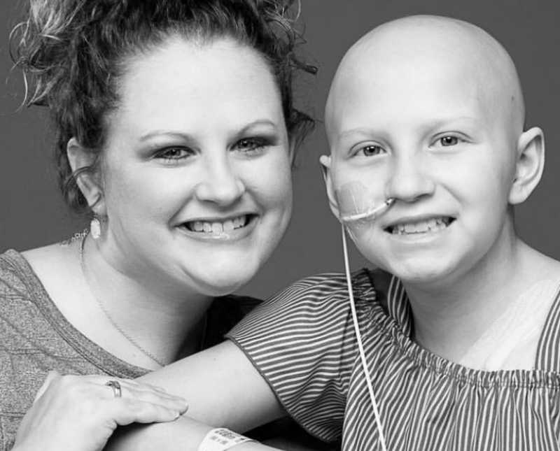 Intubated young girl with shaved head smiles beside her mother