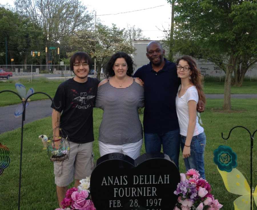 Mother stands beside her husband and two kids behind her third child's grave
