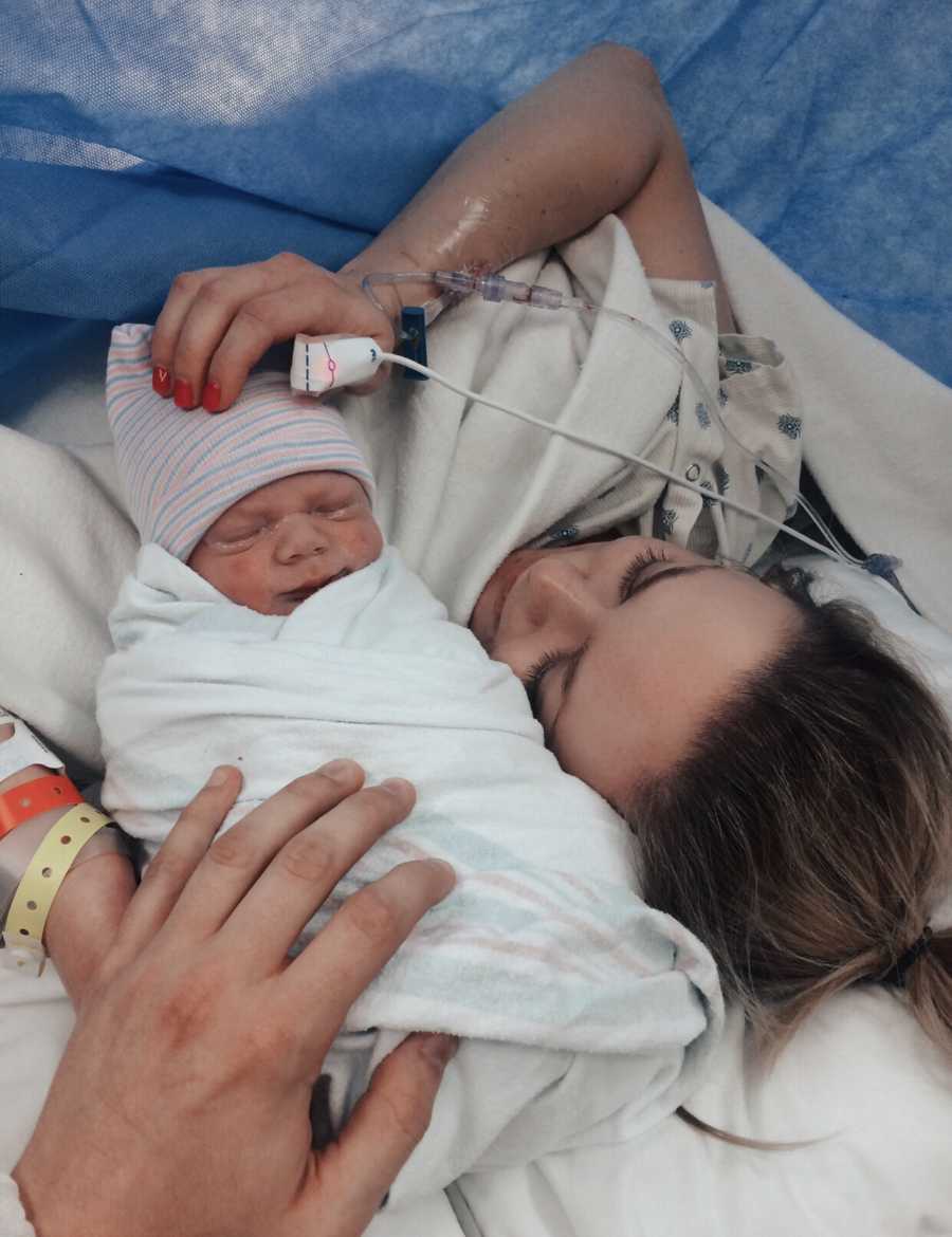 Mother with gastroparesis lays looking at newborn swaddled in blanket after c-section