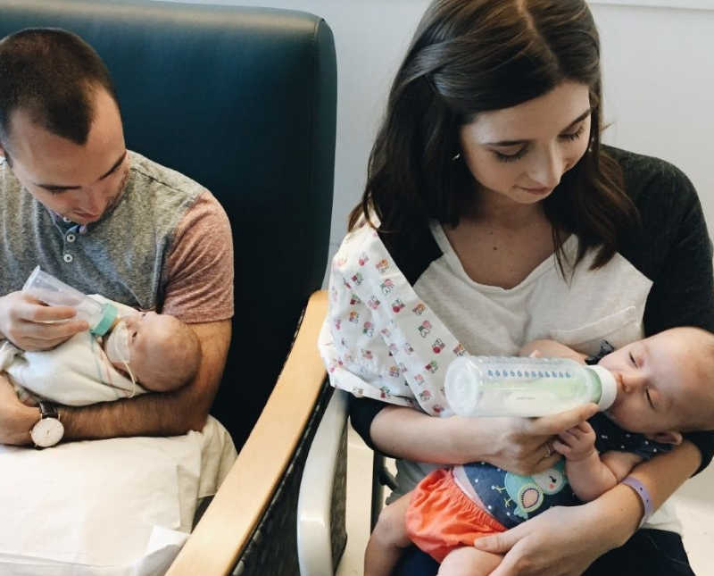 Father sits in chair bottle feeding intubated twin while mother sits beside him bottle feeding other twin