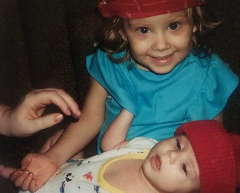 Little girl sits smiling with baby sibling in her lap