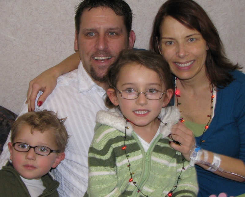 Husband and wife with illnesses smile with their two children in hospital room