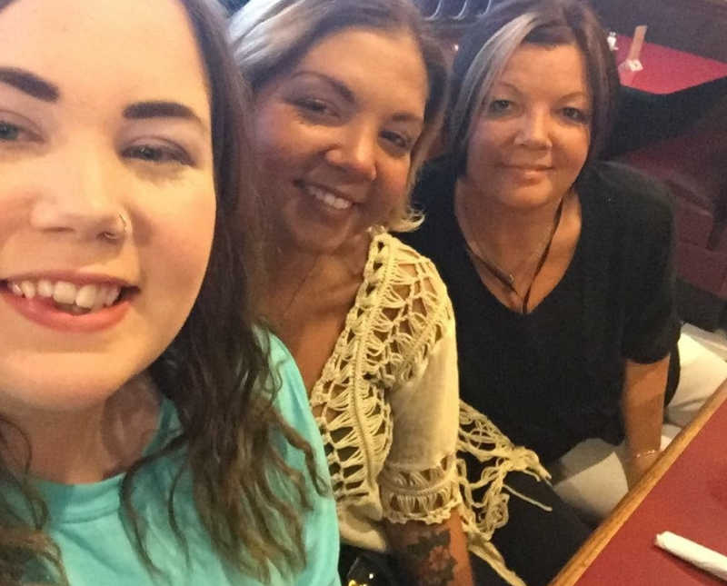 Woman smiles in selfie at restaurant table beside sister and mother