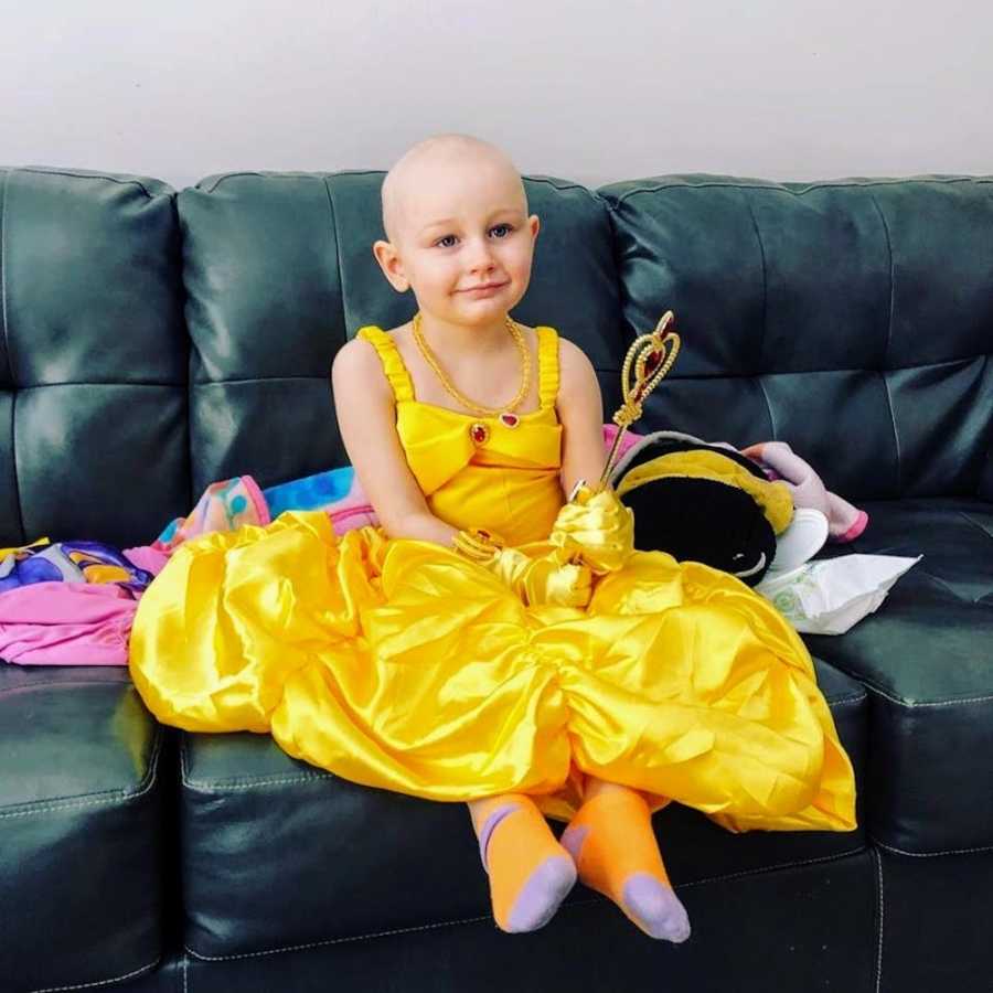 Little girl with Acute Lymphoblastic Leukemia sits on couch wearing Princess Belle dress