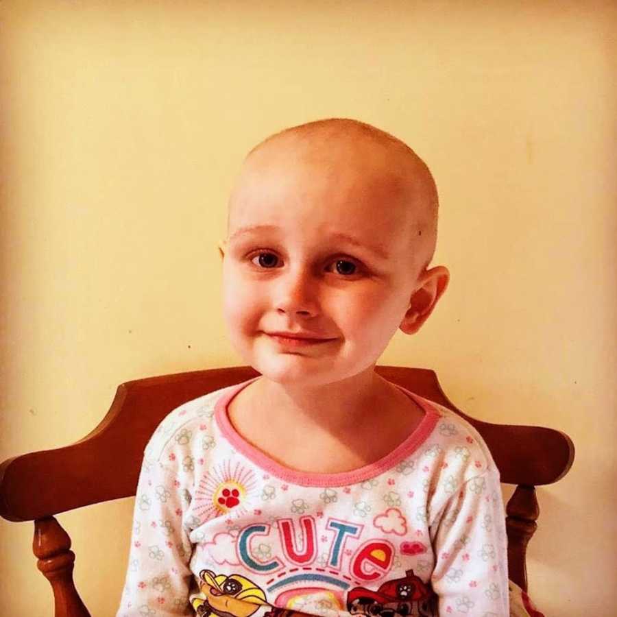 Little girl with Acute Lymphoblastic Leukemia sits in wooden chair smiling