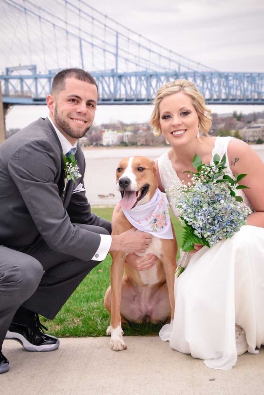 Bride and groom smile as they kneel outside beside their dog