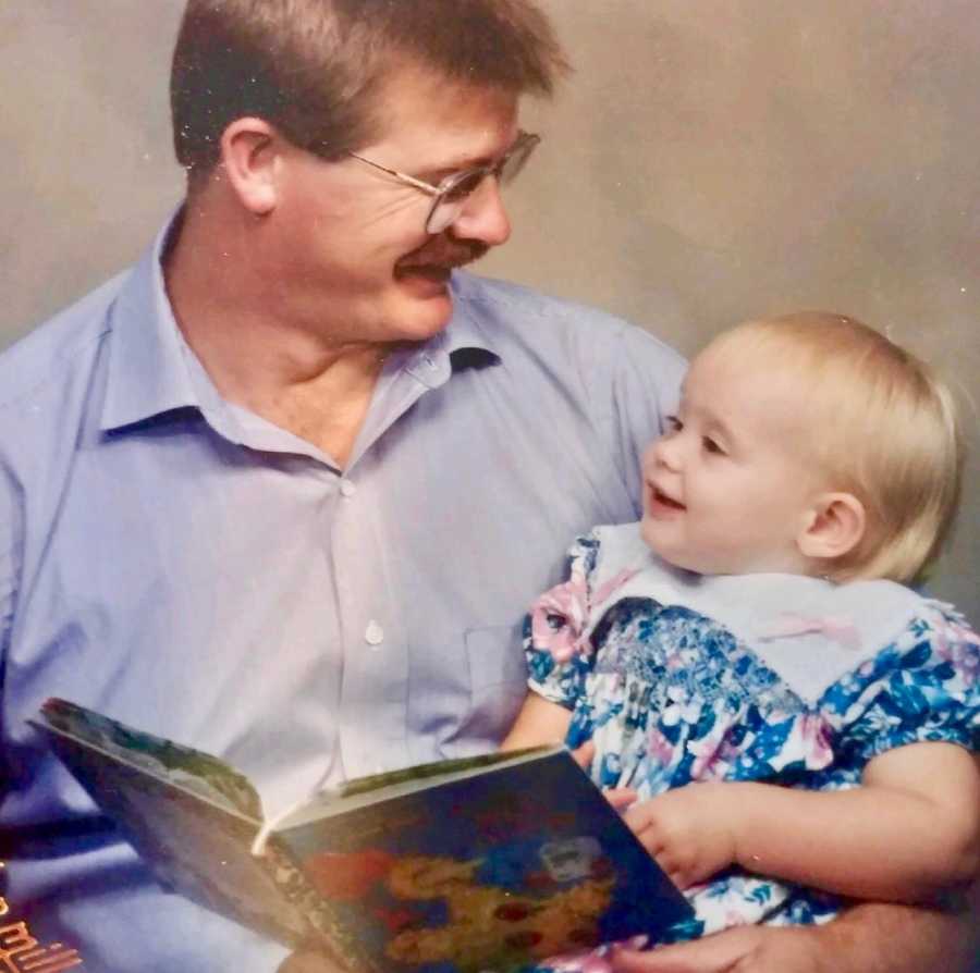 Baby girl sits in fathers lap as he reads her a book