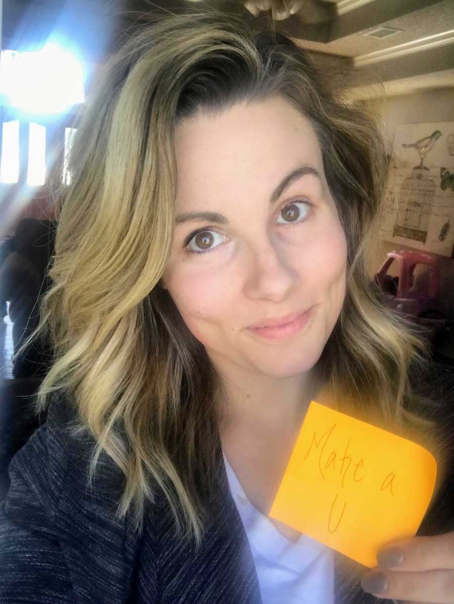 Mother smiles in selfie holding up sticky note that says, "Make A U"