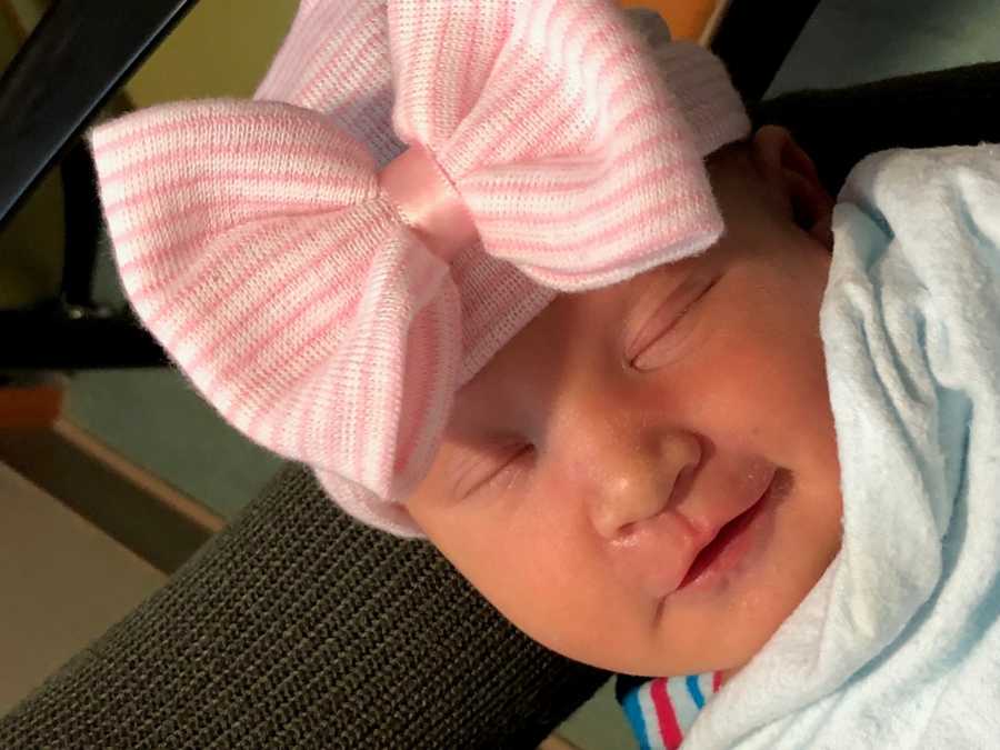 Newborn baby lays asleep with pink and white hat with large bow on it