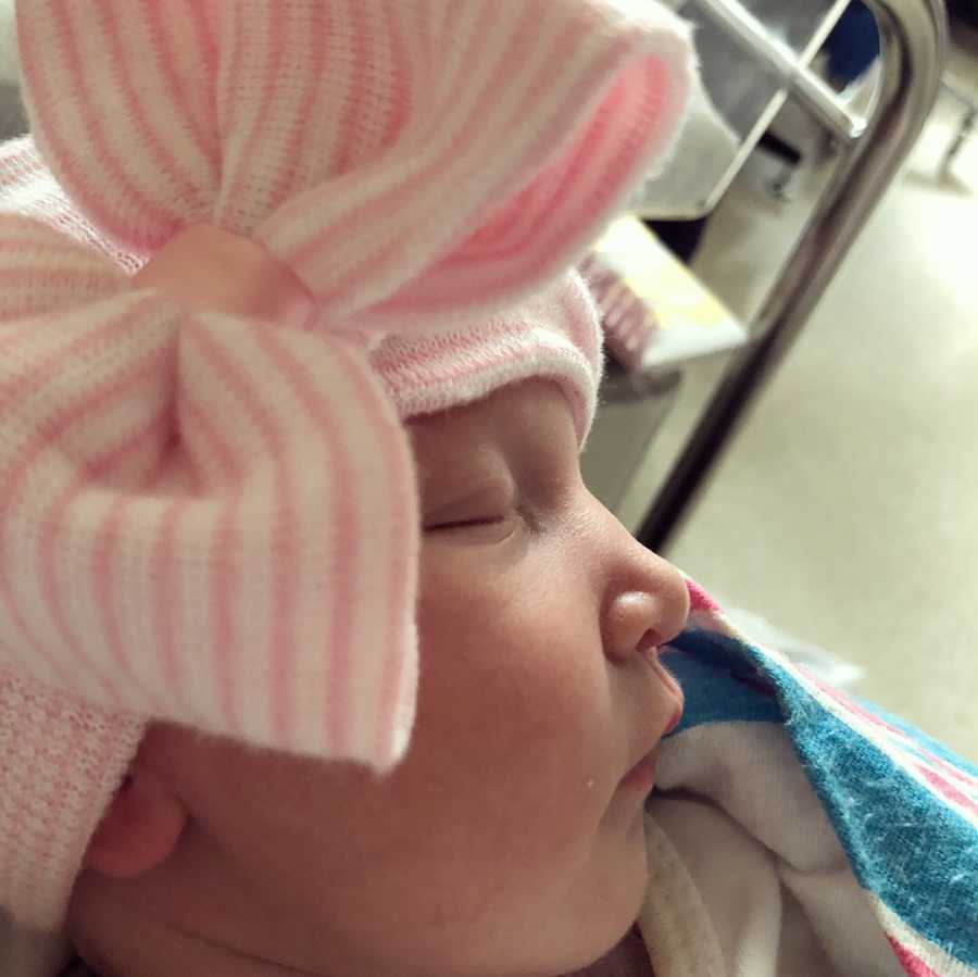 Close up of newborn baby asleep with pink and white hat with large bow on it
