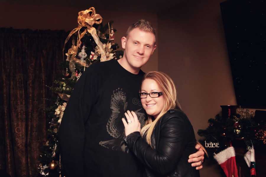 Husband and wife who struggle with fertility stand in home in front of Christmas tree