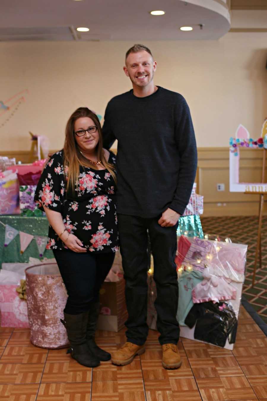 Pregnant woman stands beside her husband at their gender reveal party