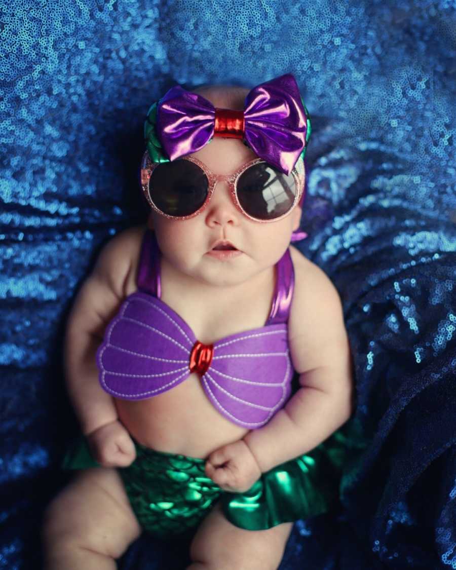 Baby lays on back in mermaid costume and sunglasses on 