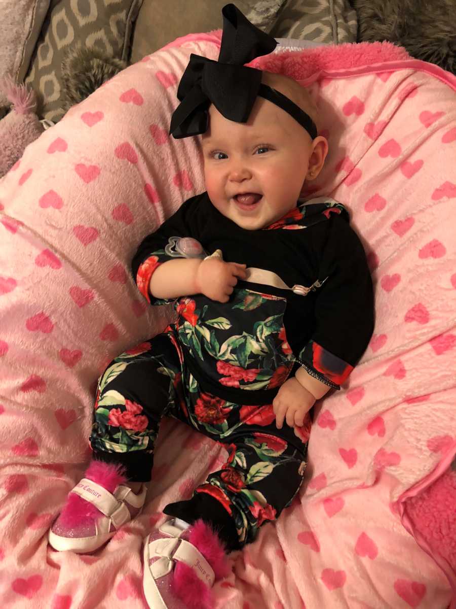 Little girl smiles as she sits on pink heart blanket with floral outfit on 