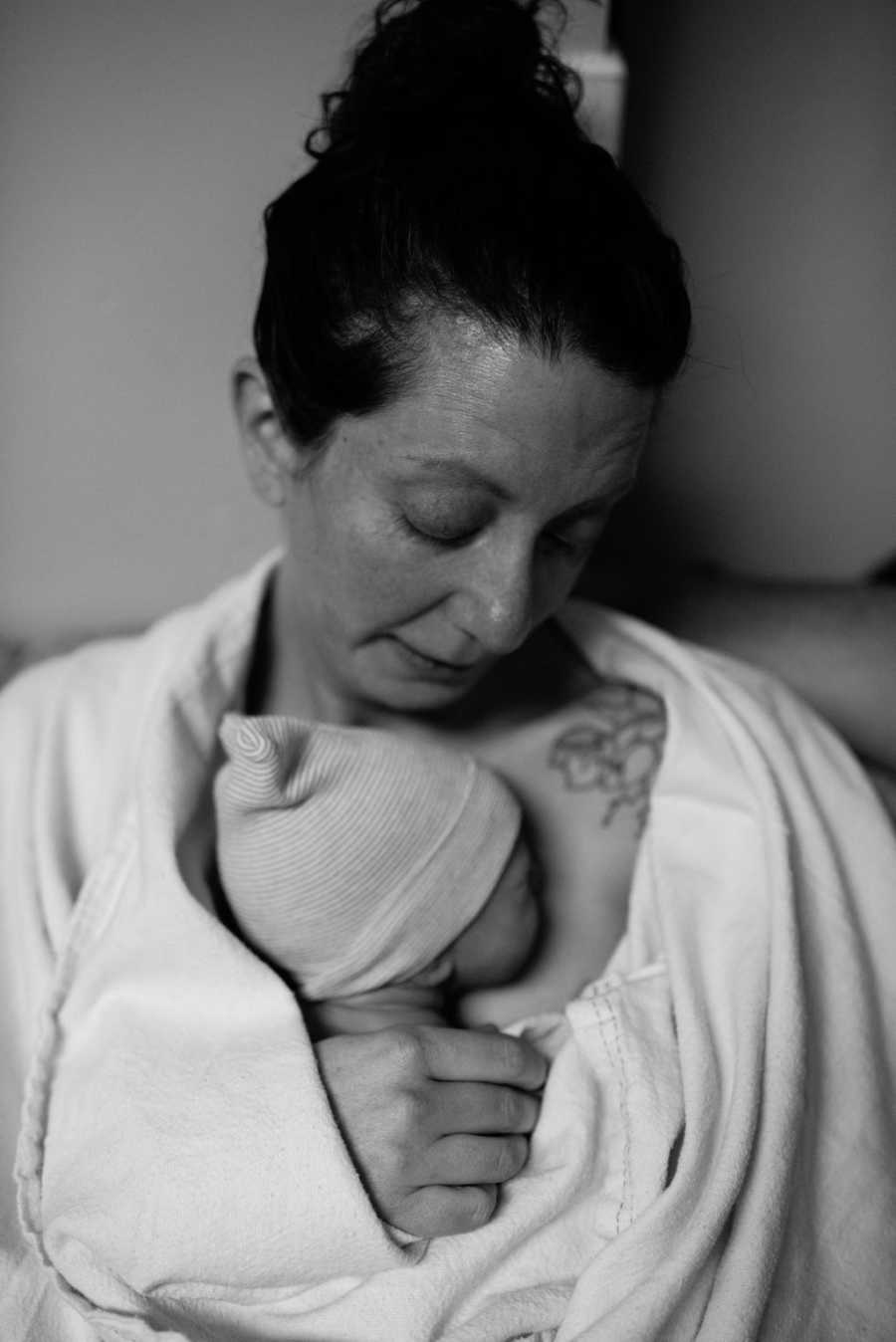 Woman looks down at adopted newborn who is laying on her bare chest