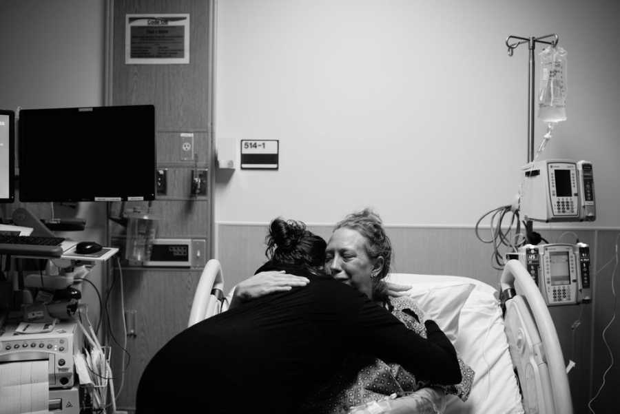 Woman sits in hospital bed hugging woman who is adopting her child