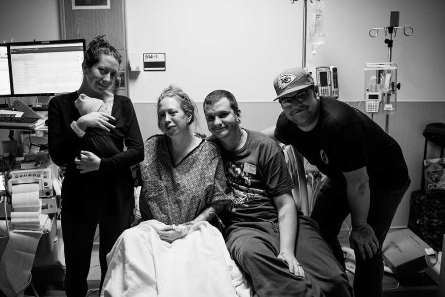 Woman sits in hospital room beside her husband and woman who adopted their child and her husband