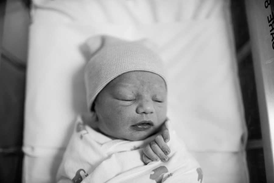 Adopted newborn lays on back asleep with hat on 