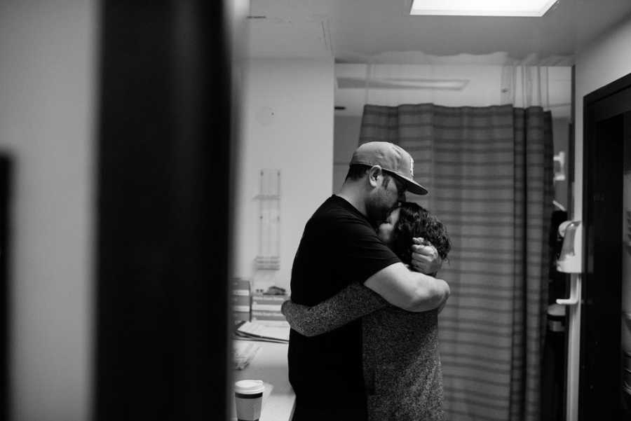 Husband and wife stand hugging in hospital room awaiting birth of adopted child