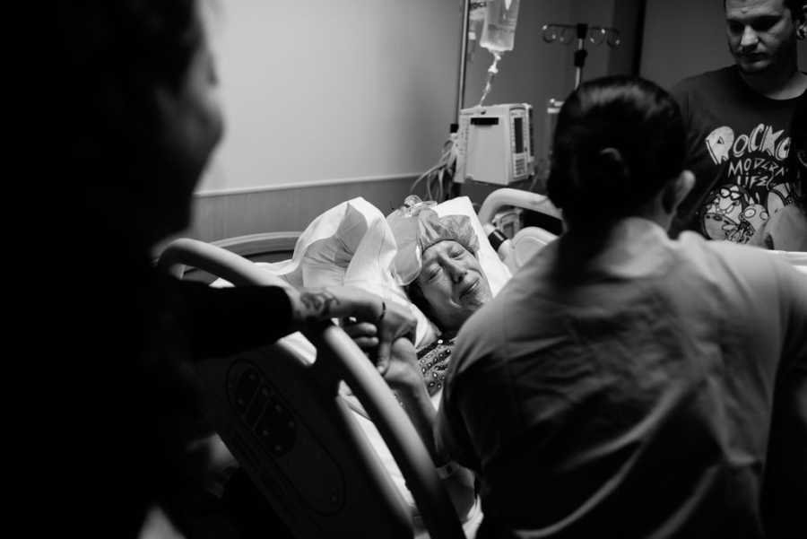Woman who is adopting newborn stands holding hands with her child's mother who lays in hospital bed