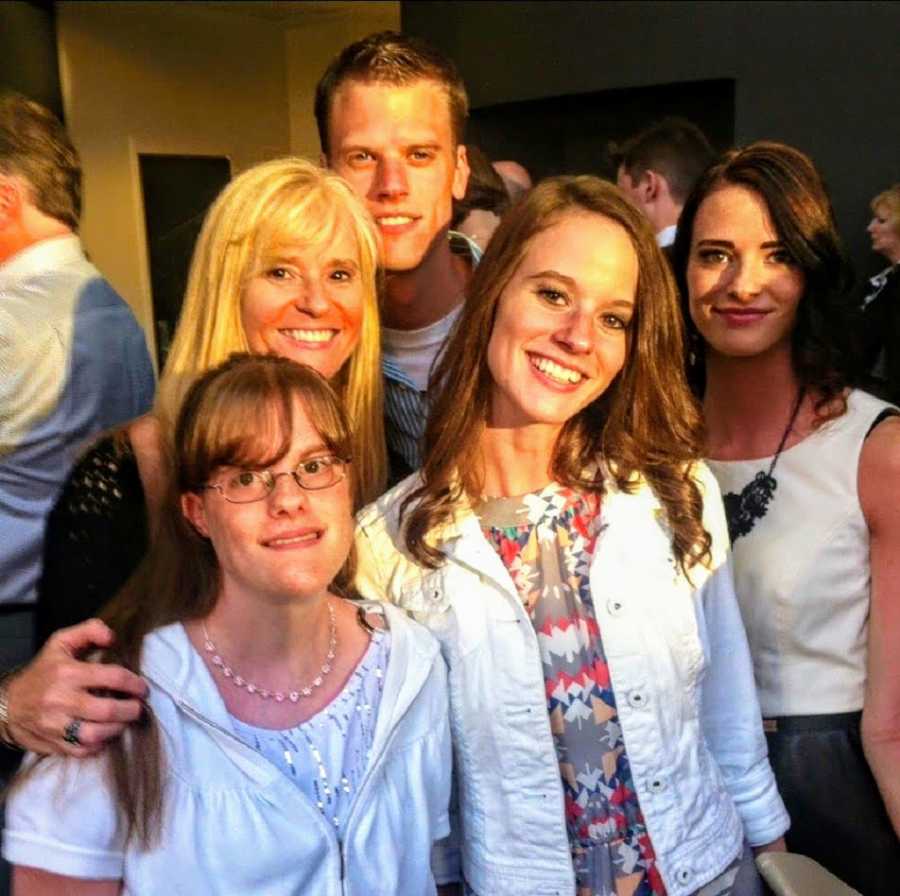 Man stands smiling outside with his mom and three sisters