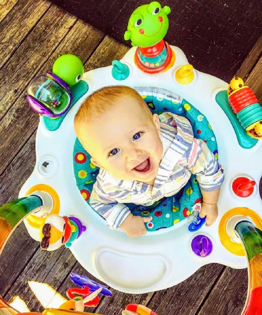 Aerial view of baby looking up smiling as he stands in baby toy