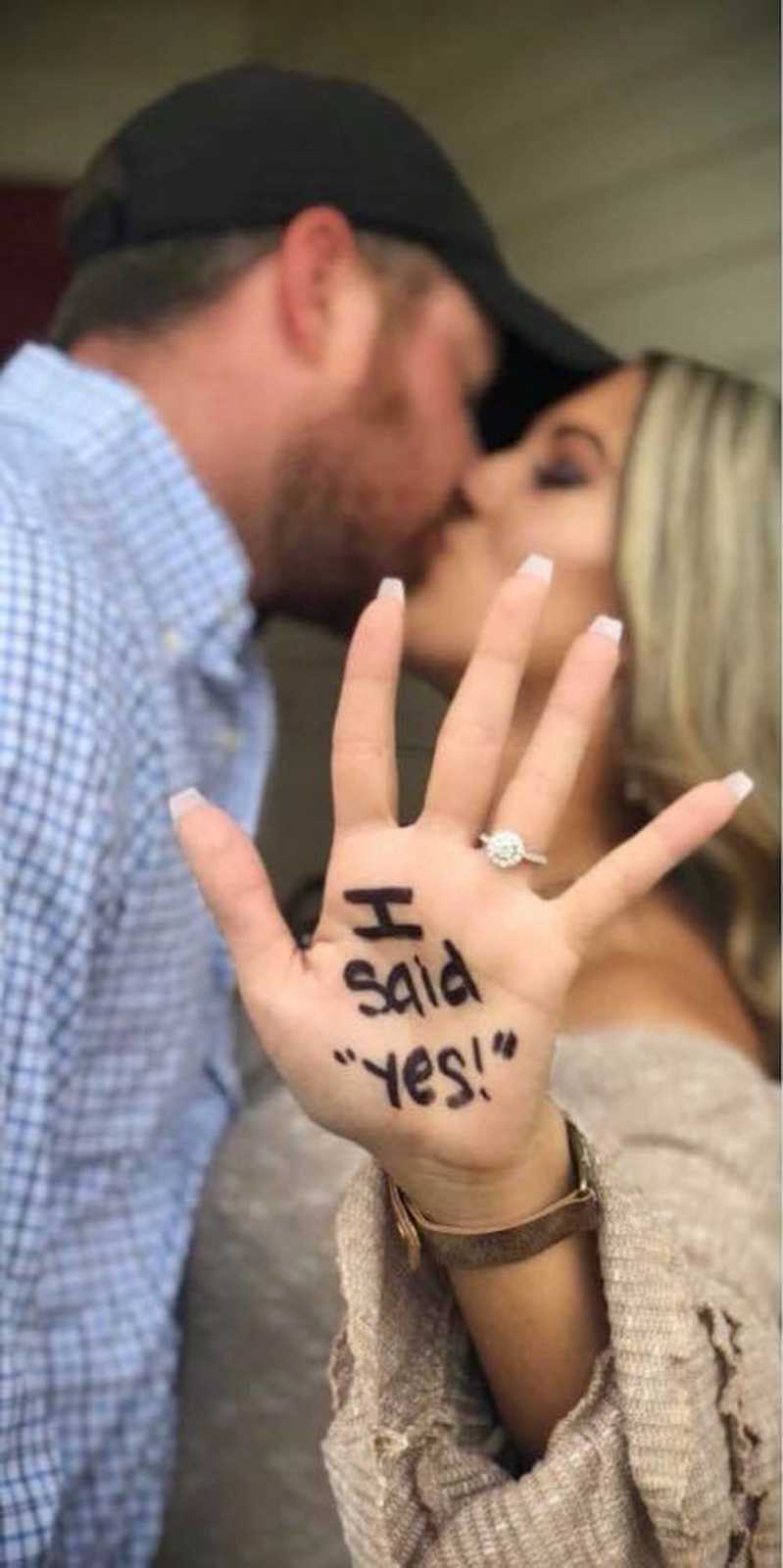 Woman kisses fiancee as she holds out her hand that says, "I said yes"