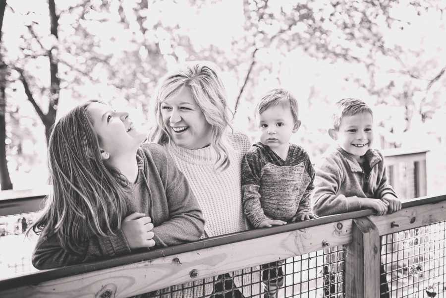 Widow stands on bridge smiling with her three children 