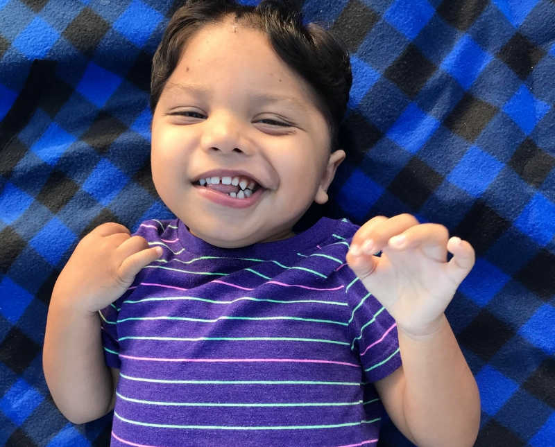Little boy with cerebral palsy lays on back smiling on blue and black check blanket