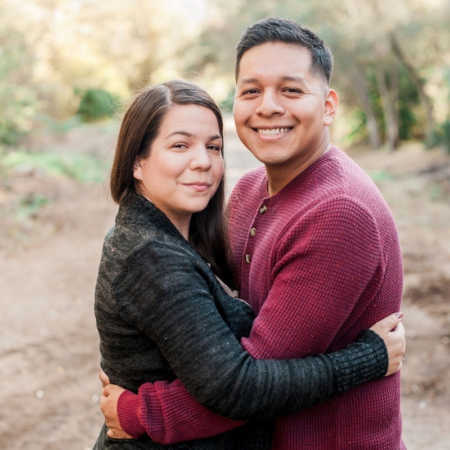 Husband and wife stand outside arm in arm smiling