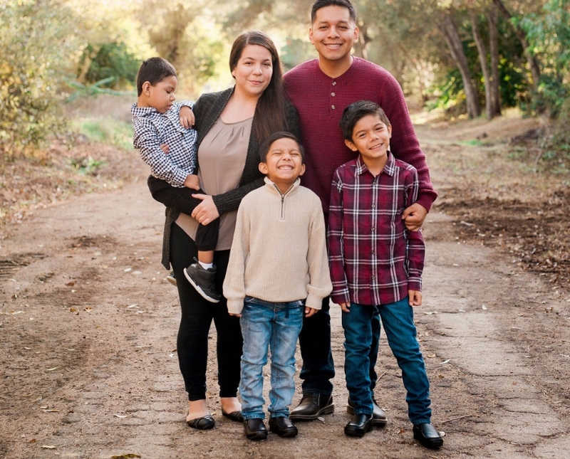 Husband and wife stand on dirt path with their two boys while mother holds son with cerebral palsy