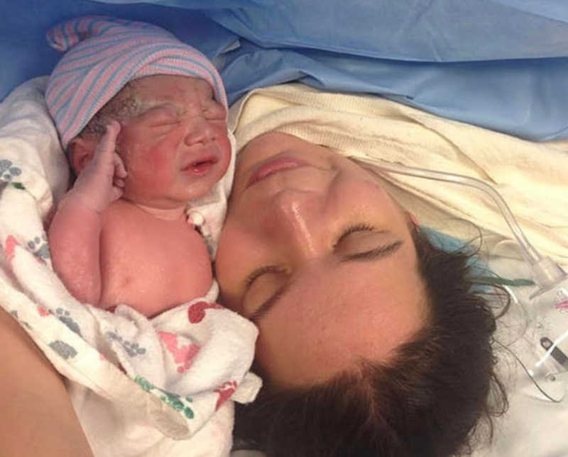 Mother lays on operating table after c-section holding newborn wrapped in hospital blanket