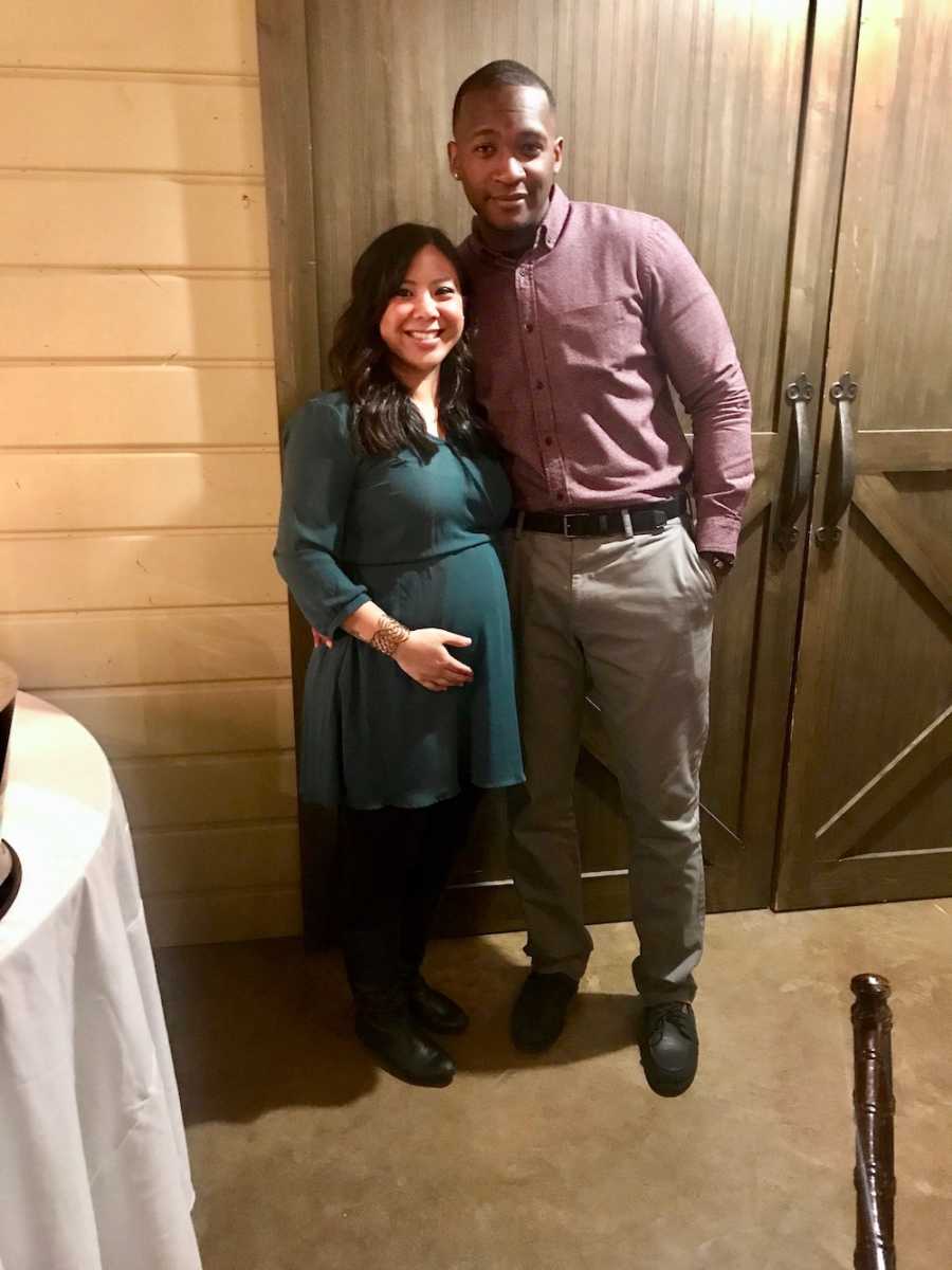 Pregnant woman stands smiling with her husband
