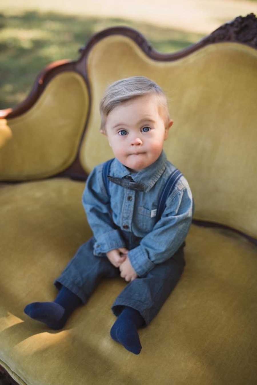 Little boy with down syndrome sits on green velvet couch wearing all denim outfit