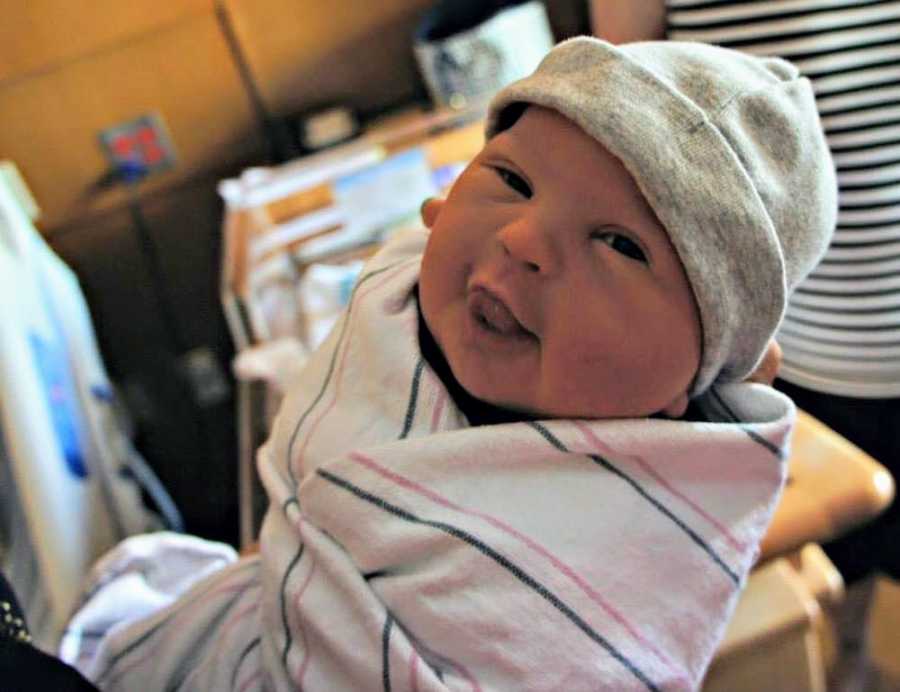 Baby boy with down syndrome smiles as he is held in air wrapped in hospital blanket