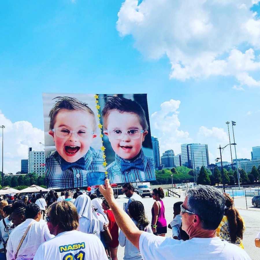 Man holds up sign that has face of down syndrome boy on it during walk