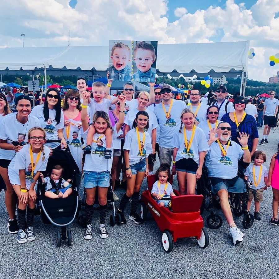 Group stands at walk for down syndrome as someone holds up sign with face of little boy with down syndrome on it