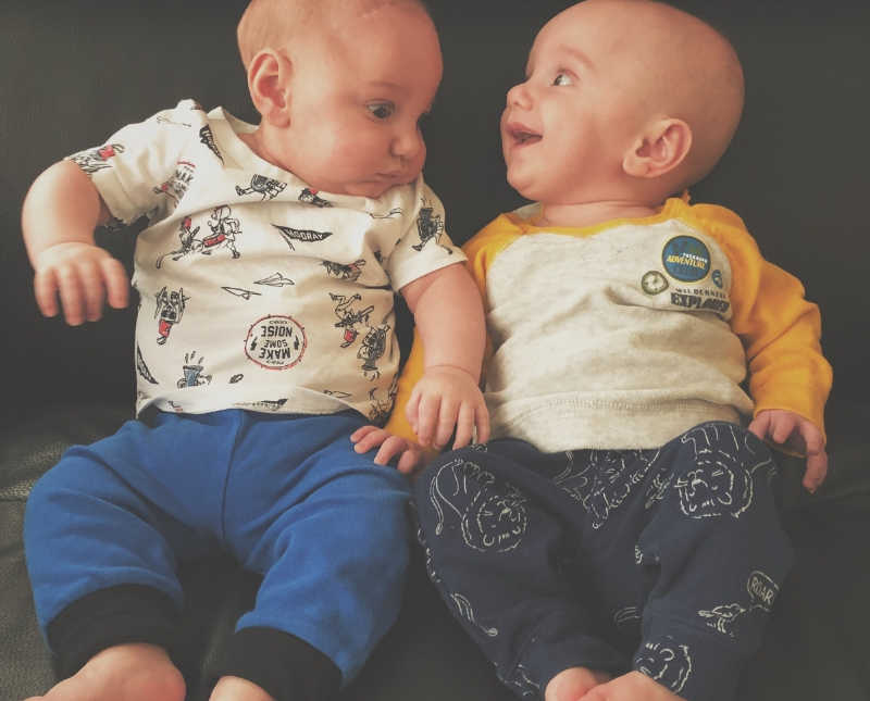 Twin baby boys sit beside each other smiling