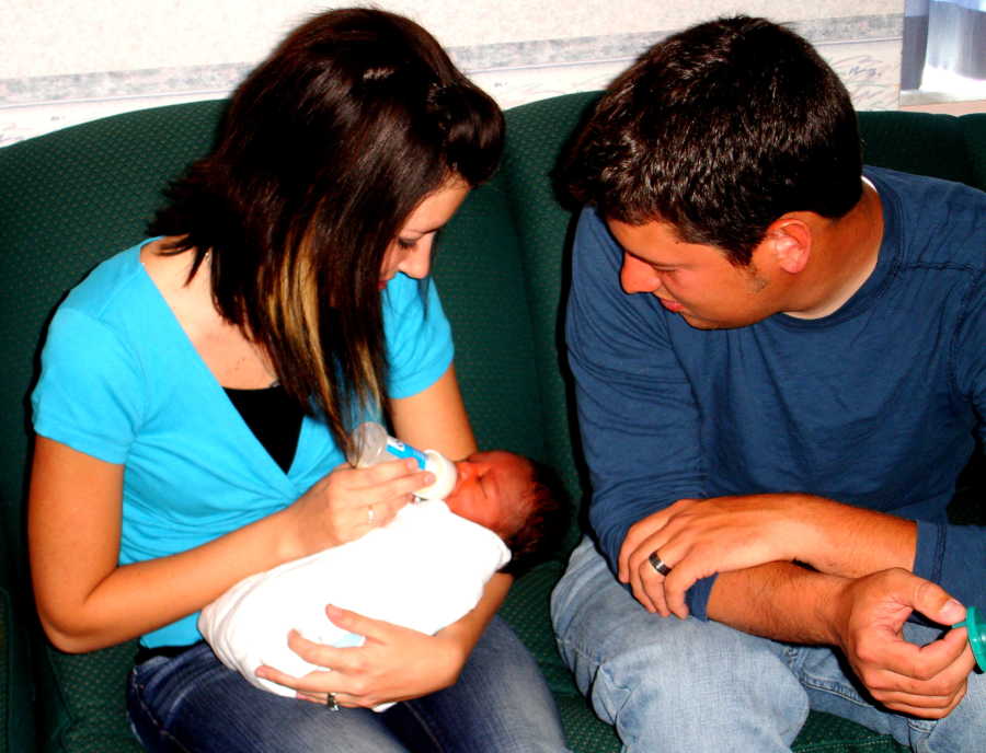 Husband and wife sit on couch as wife bottle feeds adopted newborn