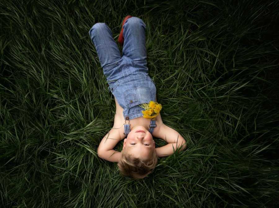Little boy with congenital heart defects lays on back in grass with arms behind his head