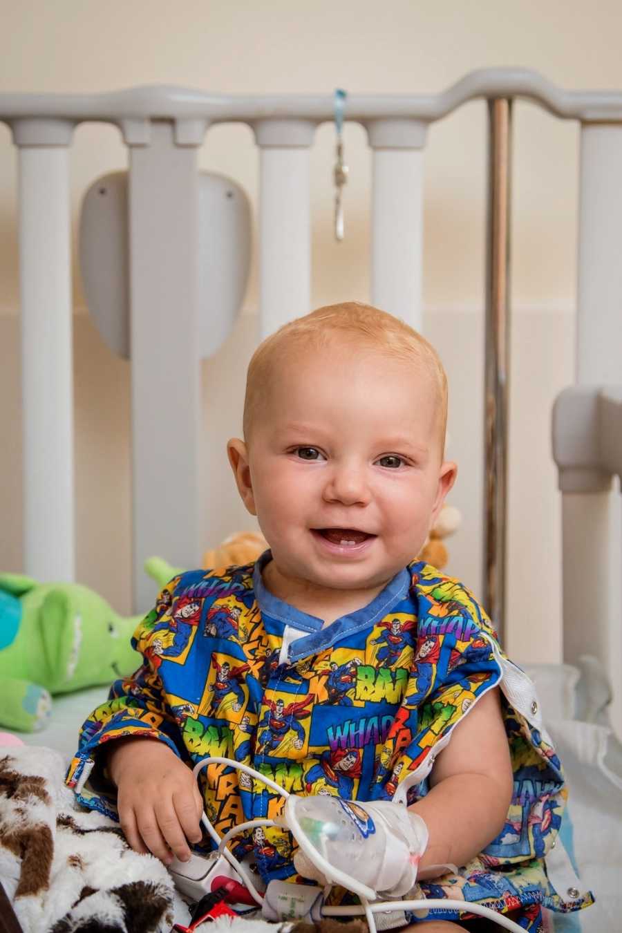 Baby boy sits smiling in hospital crib after open heart surgery 