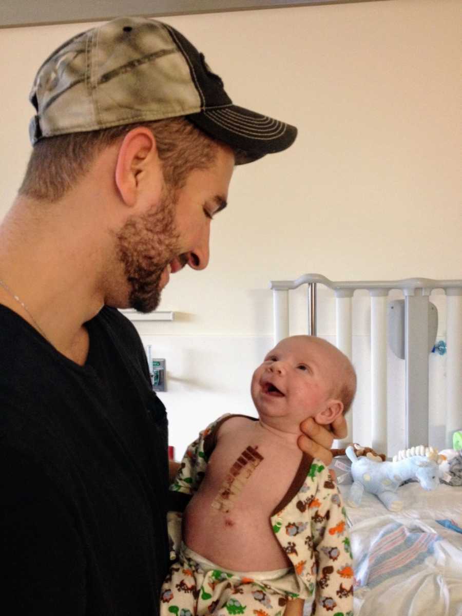 Father smiles at baby boy in his arms after he had open heart surgery