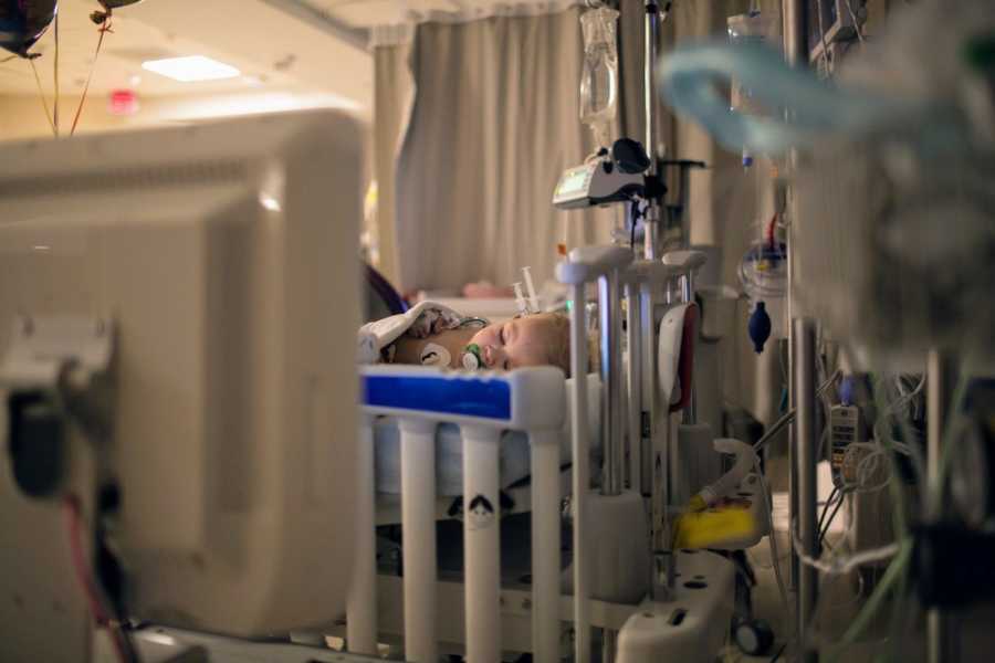 Baby boy lays in hospital crib asleep after having heart surgery