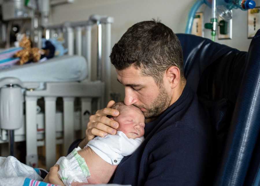 Father sits in hospital chair holding baby who needs to have heart surgery