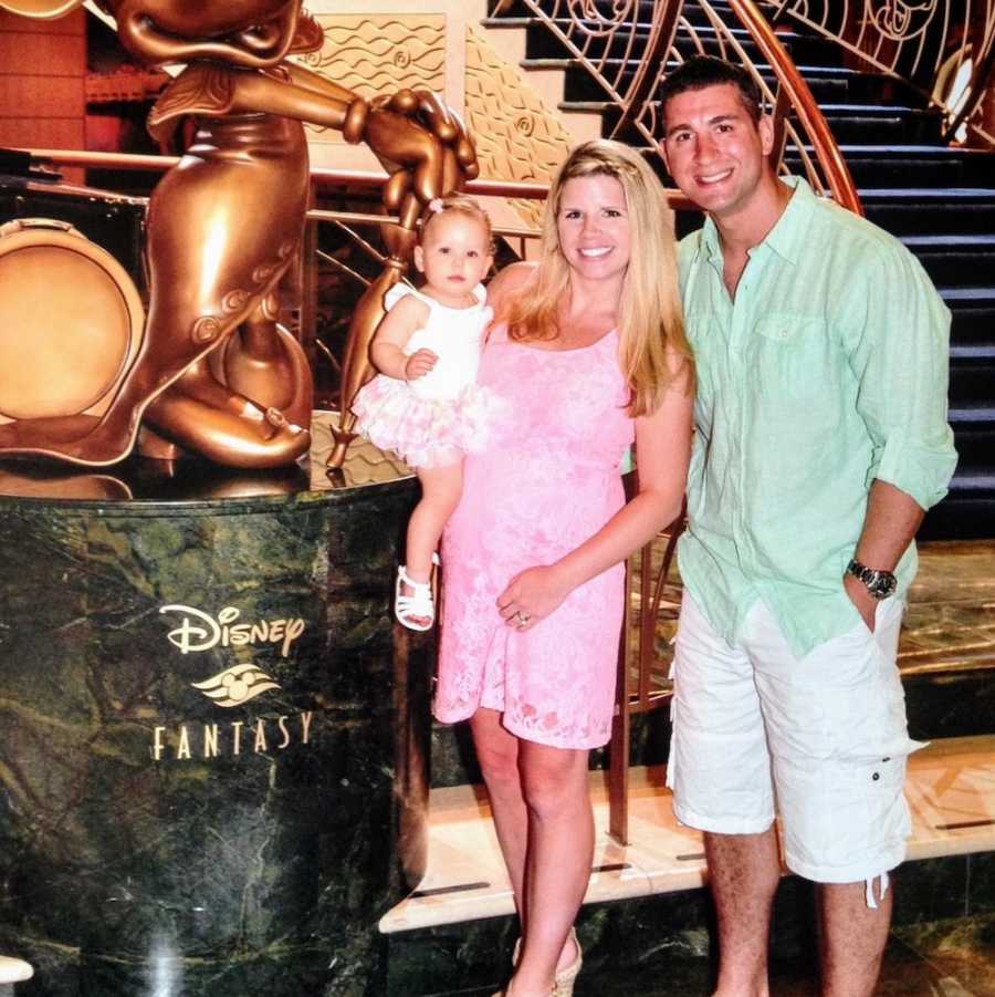 Pregnant wife stands holding her baby girl beside husband on Disney cruise
