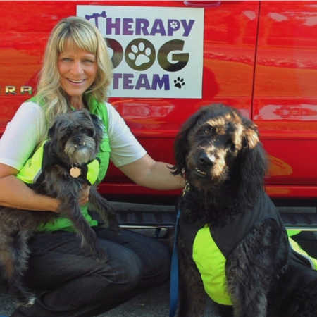 Woman with papillary thyroid carcinoma kneels beside two dogs and red car with sign "Therapy Dog Team" on it