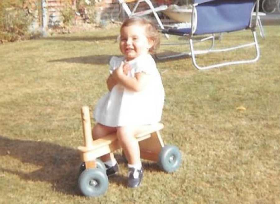 Little girl sits on scooter in yard of home