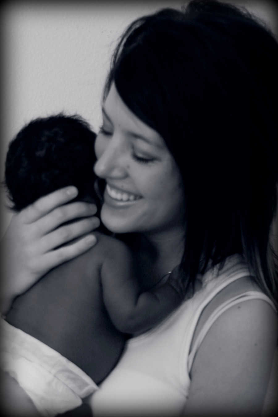 Woman smiles as she holds her adopted newborn to her chest